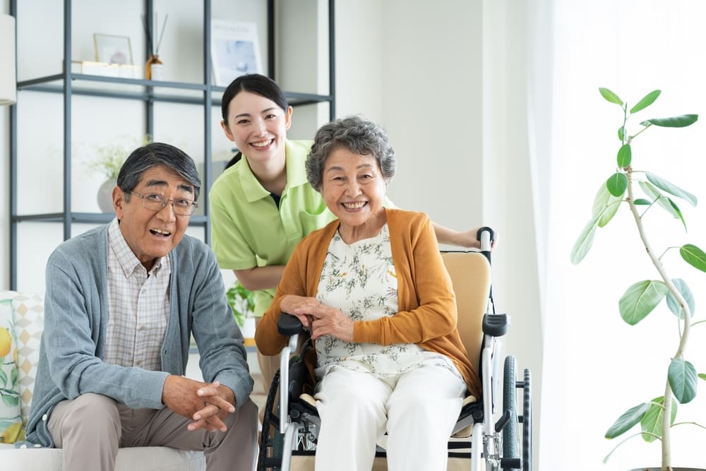 車椅子のシニアの夫婦と介護福祉士の画像
